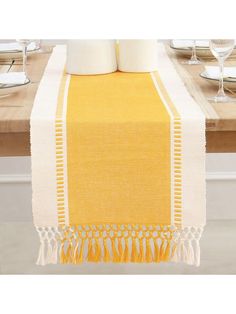 a yellow table runner with tassels on it and wine glasses in the background