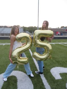 two girls are holding large balloons in the shape of numbers on a football field,