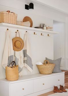 towels and baskets are hanging on the wall above a white shelf in a room with wood floors