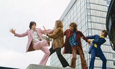 the rolling stones in front of a tall building, with one man jumping up into the air