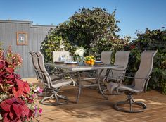 an outdoor table and chairs on a wooden deck with flowers in the vases next to it