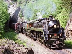 a train traveling through a lush green forest next to a rocky mountain side covered in trees