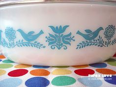 a white bowl with blue birds on it sitting on a polka dot table cloth next to a potted plant