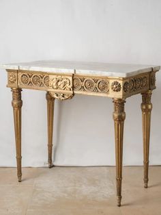 an antique console table with marble top and gold leaf decorations on the legs, against a white wall