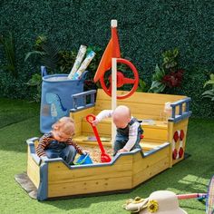 two toddlers playing in a wooden pirate ship play set on artificial grass with toys