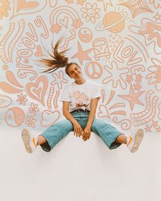 a woman sitting on top of a wall with her hair in the air and smiling