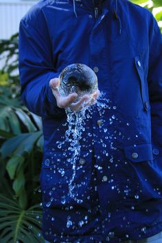 a man in blue jacket holding up a glass ball with water coming out of it