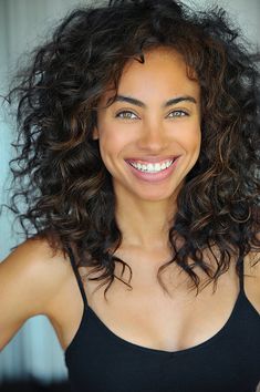 a woman with curly hair smiling and wearing a black tank top