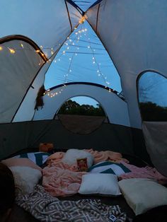 the inside of a tent with pillows and blankets on it at night, lit up by fairy lights