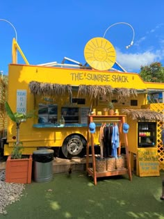 a yellow food truck parked on top of a lush green field next to a blue sky