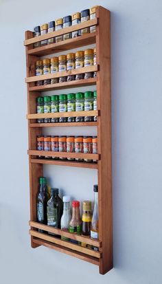 a wooden spice rack with spices and condiments on the top, against a white wall