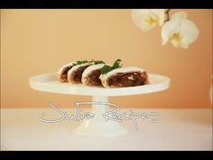 some food is sitting on a white cake plate and there are flowers in the background