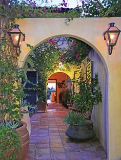 an archway leading into a courtyard with potted plants and hanging lights on either side