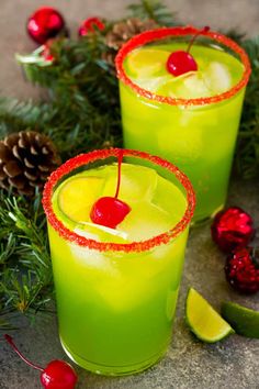 two glasses filled with green liquid next to pine cones and cherries on the table