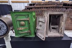 three different types of safes on display in a warehouse or workshop area, one is green and the other is brown