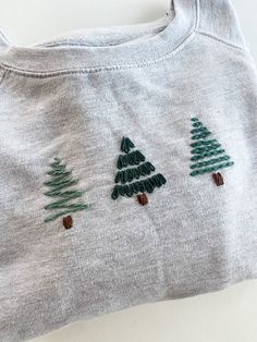 three embroidered christmas trees on a gray sweatshirt with green thread and pine cones in the center