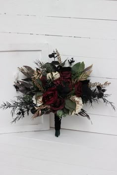 a bridal bouquet with red roses and greenery hangs on the side of a white door