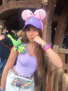 a girl in a purple shirt and hat with a green frog on her head standing next to a wooden fence