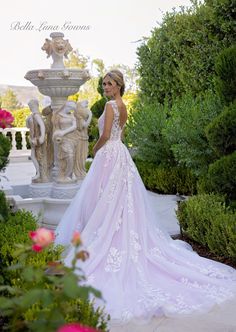 a woman in a wedding dress standing next to a fountain with flowers around her and looking at the camera