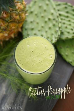 a green smoothie in a small glass next to a pineapple