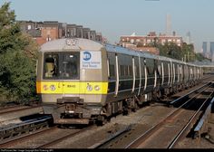 a train traveling down tracks next to tall buildings in the background with trees on either side