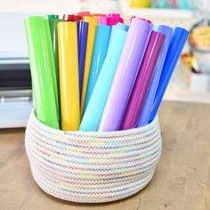 a basket filled with lots of colorful straws on top of a wooden table next to a laptop