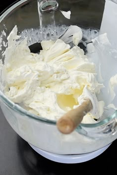 a mixing bowl filled with whipped cream on top of a black counter next to a wooden spoon