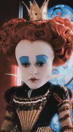 a close up of a doll with red hair wearing a crown and blue eyeshade