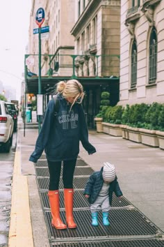 a woman and child are walking down the sidewalk in rain boots on a rainy day