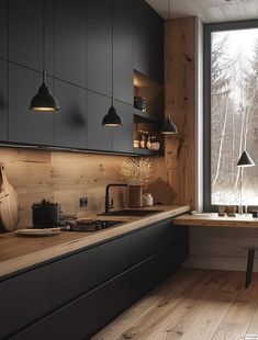 a kitchen with black cabinets and wooden floors, along with an open window that looks out onto the woods