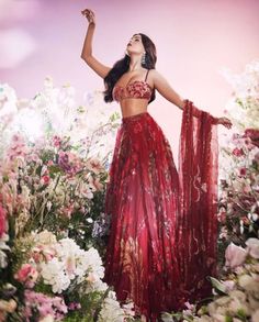 a woman wearing a red dress standing in flowers with her arms raised up to the sky