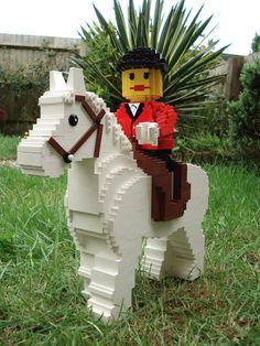 a lego man riding on the back of a white horse in a grassy area next to a palm tree