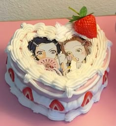 a heart shaped cake decorated with two people and a strawberry on top, sitting on a pink table