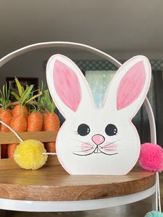 a white bunny mask sitting on top of a wooden table next to carrots and plants