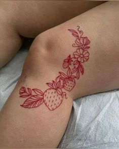 a woman laying on top of a bed with a strawberry tattoo on her arm and leg