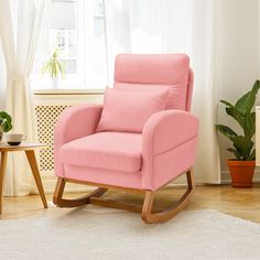 a pink rocking chair sitting in front of a window next to a potted plant