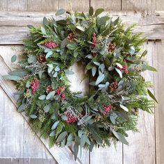 a wreath is hanging on the side of a wooden door with greenery and berries