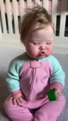 a baby sitting on the floor playing with a green object