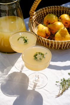 two glasses filled with drinks sitting on top of a table next to baskets of fruit