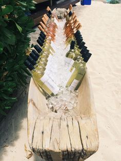 several bottles of wine sitting on top of a wooden bench in the sand near some bushes