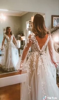 a woman standing in front of a mirror wearing a wedding dress with long sleeves and open back