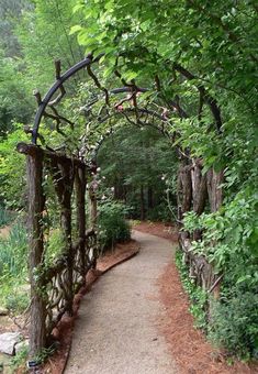 a path in the middle of a forest with an arch made out of branches and flowers