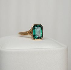 an emerald colored ring sitting on top of a white display stand with a white background