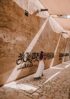 a woman in a white dress standing next to a wall with arabic writing on it