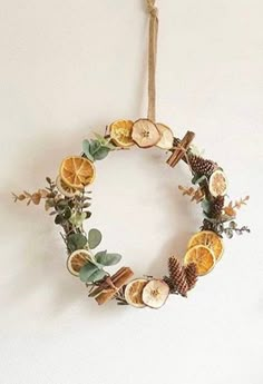 a wreath made out of oranges and pine cones hanging on a wall with rope