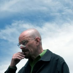 a bald man with glasses talking on a cell phone in front of a blue sky