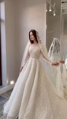 a woman standing in front of a mirror wearing a wedding dress with long sleeves and a veil