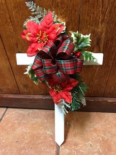 a cross decorated with poinsettis and greenery is on the ground next to a door