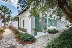 a small white house with green shutters on the front and side doors, surrounded by trees