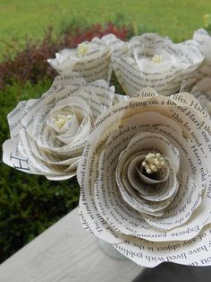 some paper flowers sitting on top of a wooden table in front of grass and bushes